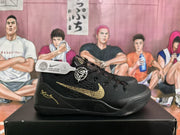 Side view of black Nike basketball sneakers with gold Swoosh detailing and a circular side emblem on a black shoebox.