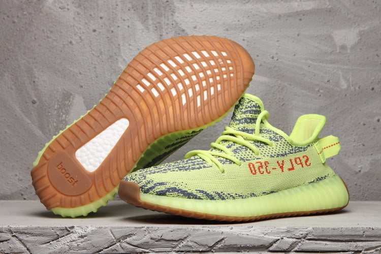 Lime green 350 V2 sneakers shown from the side with one shoe lifted to reveal the gum-colored outsole.