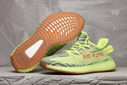 Lime green 350 V2 sneakers shown from the side with one shoe lifted to reveal the gum-colored outsole.