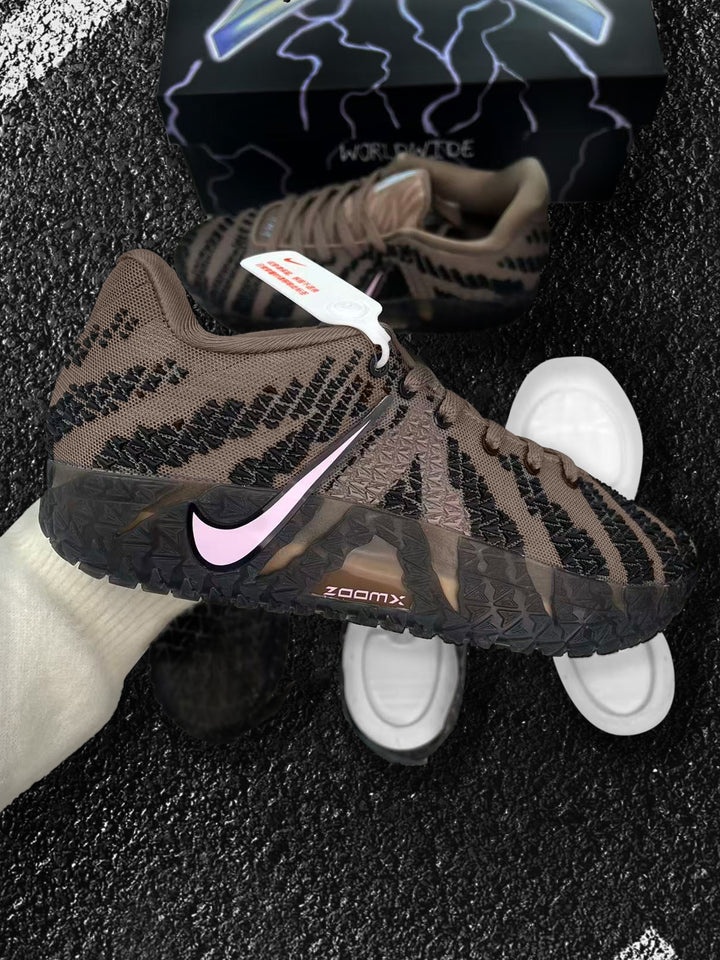 Brown and black Nike sneaker with a pink Swoosh, shown beside a second shoe and white outsole components.