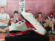 White, red, and black low-top sneaker shown at an angle, with perforated panels.