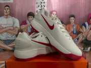 Angled view of paired white Nike sneakers showing the red Swoosh, white uppers and red rubber outsoles.