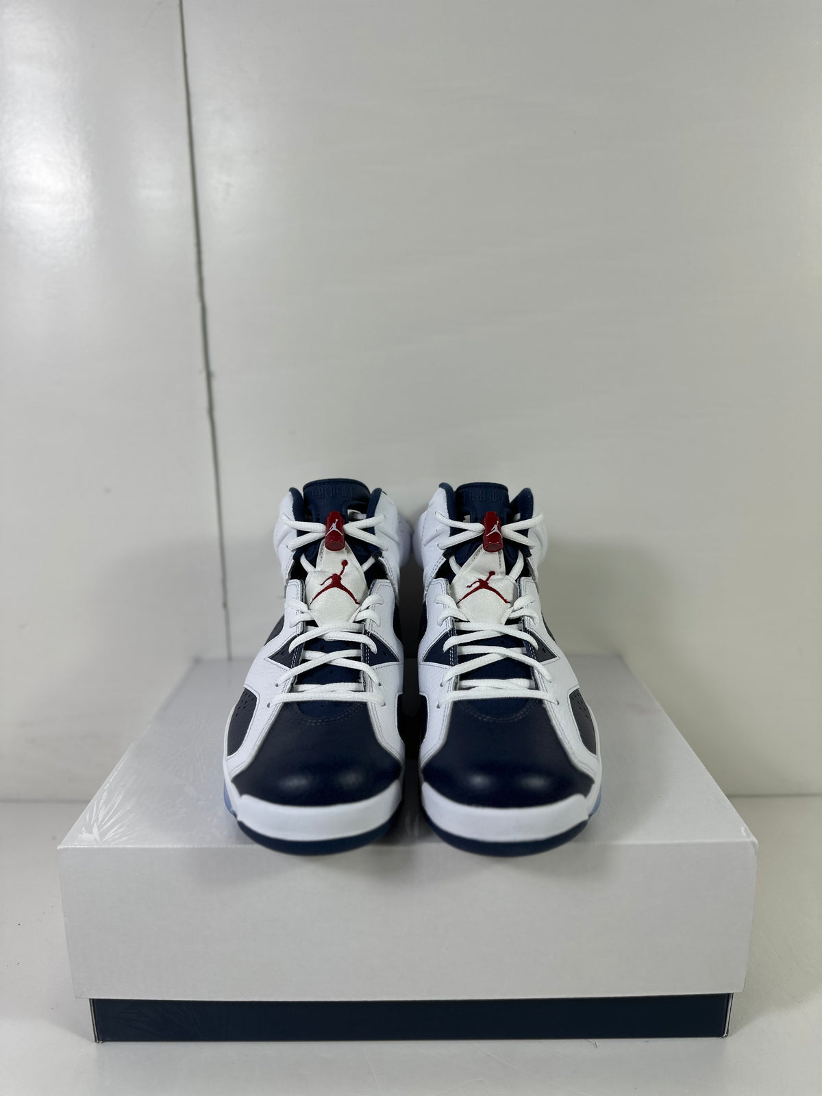 Front view of white and navy high-top Jordan Air Jordan 6 Retro sneakers displayed on a shoebox.