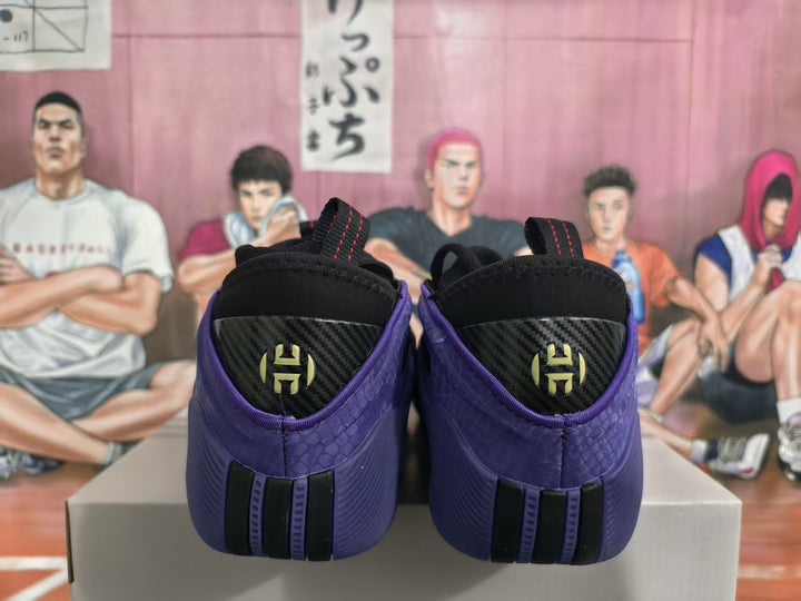 Rear view of purple basketball sneakers showing black heel panels, gold-colored heel emblems, and red-stitched pull tabs.