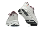 Rear and outsole views of white and mauve On Cloudmonster 3 shoes.