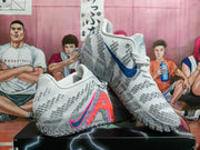 Angled view showing the gray and white sneakers, blue and multicolor side graphics, textured panels, and patterned outsole.