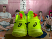 Rear view of the fluorescent green shoe pair showing ASICS heel branding and red pull tabs.