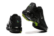 Rear and outsole views of black Nike Air Max Plus sneakers with neon yellow-green outsole accents.