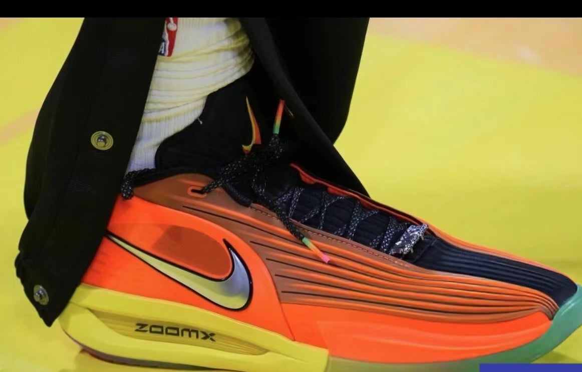 Close-up of an orange Nike athletic sneaker with navy laces and upper details, green accents, a visible Swoosh, and ZoomX marking.