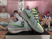 Angled view of blue-green Nike basketball sneakers showing perforated side panels, layered overlays, lime accents, and light-colored soles.