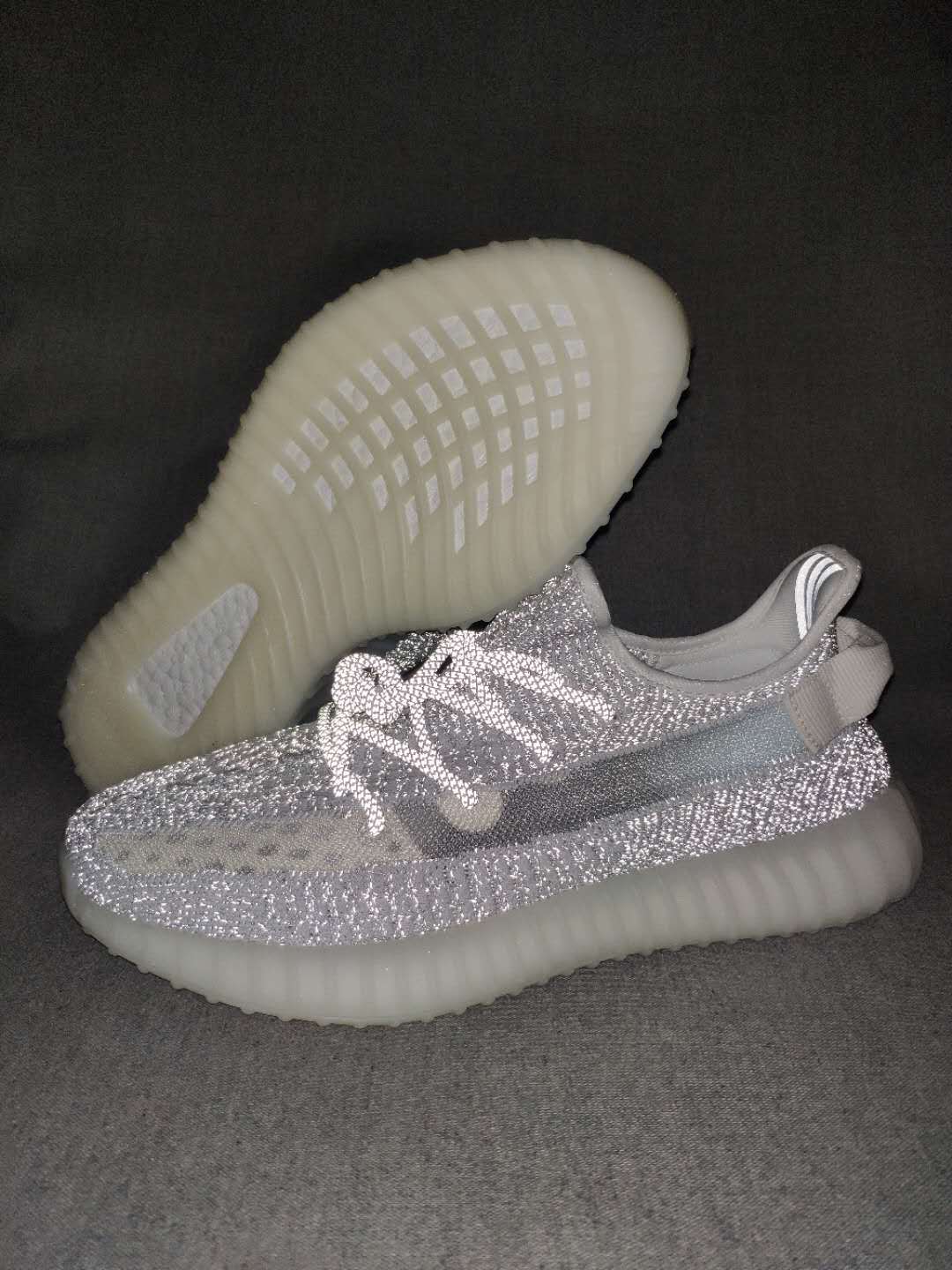 Close-up view of silver-gray Yeezy 350 V2 sneakers showing the textured upper, side stripe, laces, and translucent sole.