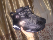 Pair of black high-top sneakers held against a curtain, showing reflective-style laces and side perforations.