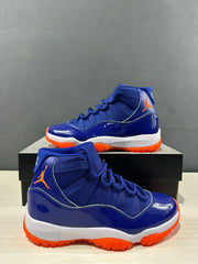 Close product view showing blue textile-like upper panels, glossy blue overlays, orange branding, and orange outsole accents.