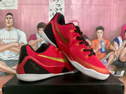 Angled view of the red and gold Nike basketball sneakers showing the side branding, black heel panels, patterned accents, and white outsoles.