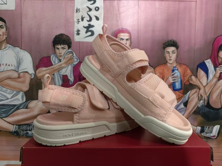 Pair of pink New Balance sandals displayed at an angle, showing the adjustable straps, open toes, textured uppers and light-colored soles.