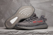 Pair of dark grey and black patterned Yeezy 350 V2-style sneakers showing the ribbed outsole and red side lettering.