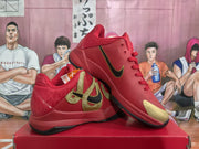 Angled view of two red Nike basketball sneakers, highlighting the gold-and-black side branding, gold toe accents, and black outsole.