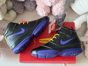 Pair of black and purple high-top sneakers displayed on a red box, with an additional lace set visible.