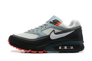 Side view of a gray, black and white Nike-branded sneaker with coral outsole accents and a visible heel air unit.