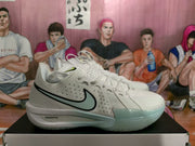 Side view of a white Nike basketball sneaker showing the black Swoosh, lace-up construction, pale green outsole tint, and ZoomX midsole branding.