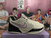Side view of a beige basketball sneaker with black trim and a pink-accented side logo
