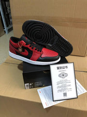 Black and red low-top sneaker shown with its black patterned rubber outsole facing upward, beside a shoebox and printed document.