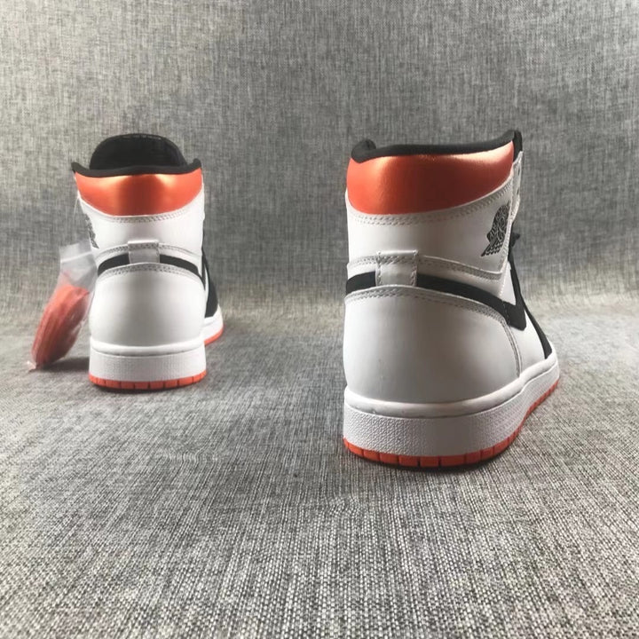 Rear view of white, black, and orange high-top Jordan sneakers on a gray fabric background.