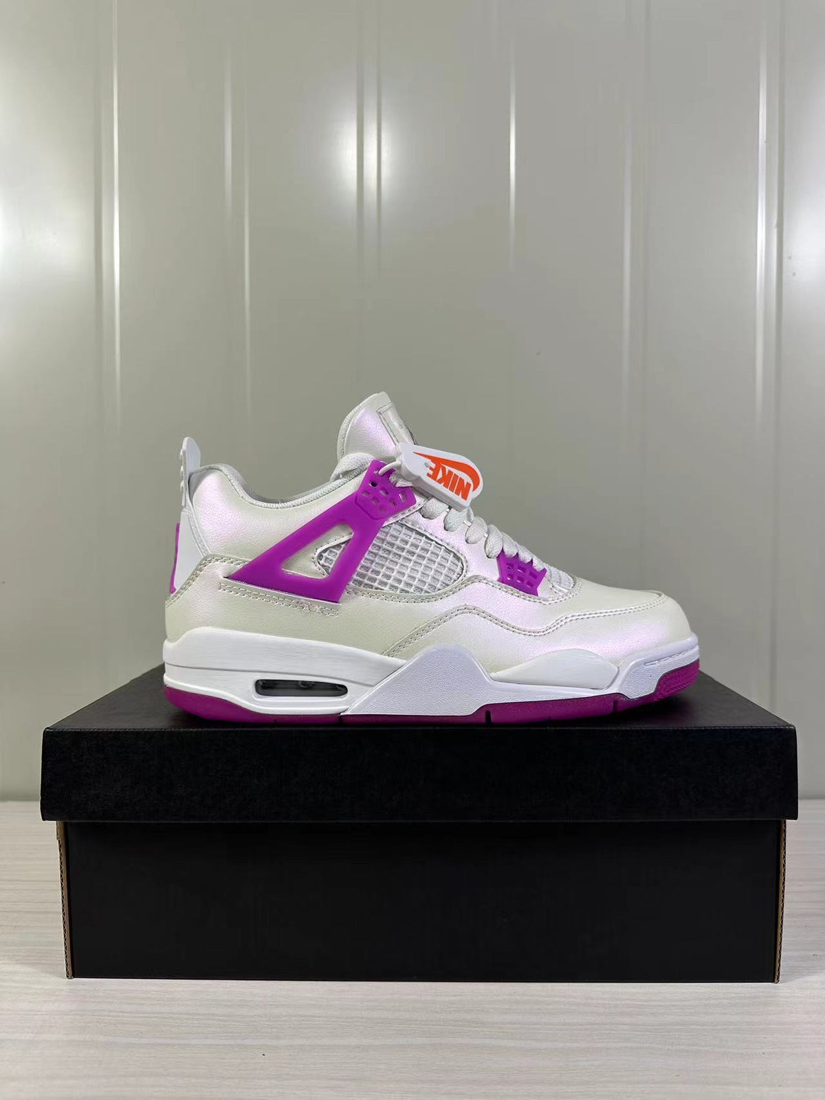 Side view of white and Hyper Violet Jordan Air Jordan 4 Retro sneakers displayed on a black shoebox.