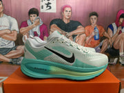 Side profile of a gray Nike running shoe with green accents, black swoosh branding, and visible ZoomX text on the sole.