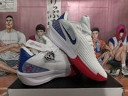 Angled view of white Nike basketball shoes with blue side accents and red outsole sections.