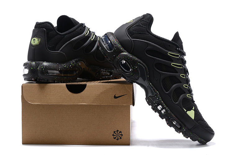 Black Nike Air Max Plus sneakers with lime accents displayed on a shoebox