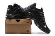 Black Nike Air Max Plus sneakers with lime accents displayed on a shoebox