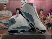 Angled view of the blue-gray and white sneaker pair showing perforated side panels, rounded heel details, and contrasting segmented outsoles.