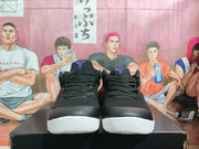Front view of black low-top basketball sneakers with purple tongue branding and white outsoles.