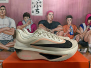 Side profile of a beige Nike running shoe with a black swoosh, pink accent trim, and visible ZoomX midsole branding.