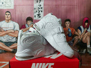Angled view of white Nike high-top sneakers highlighting the strap, perforated side panels, layered sole design, and heel air unit.