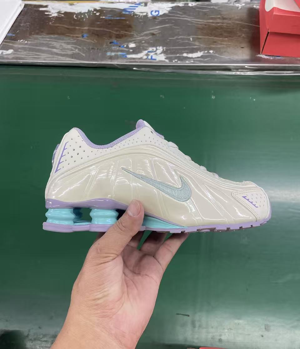 Side view of a cream youth sneaker with a light blue Swoosh, lavender accents, and visible heel cushioning.