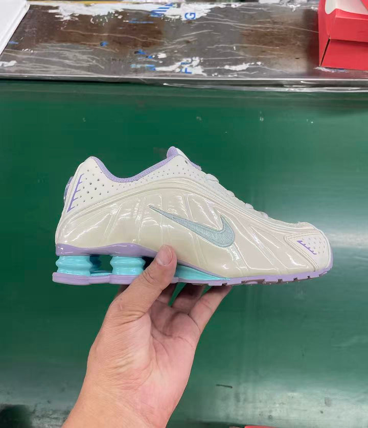 Side view of a cream youth sneaker with a light blue Swoosh, lavender accents, and visible heel cushioning.