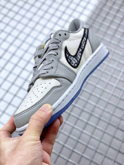 Angled close-up showing grey overlays, white perforated toe panel, patterned black Swoosh, and grey laces.