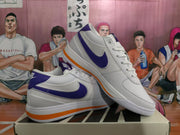 Angled view of two white Nike sneakers highlighting the blue-purple side branding and orange outsole accents.