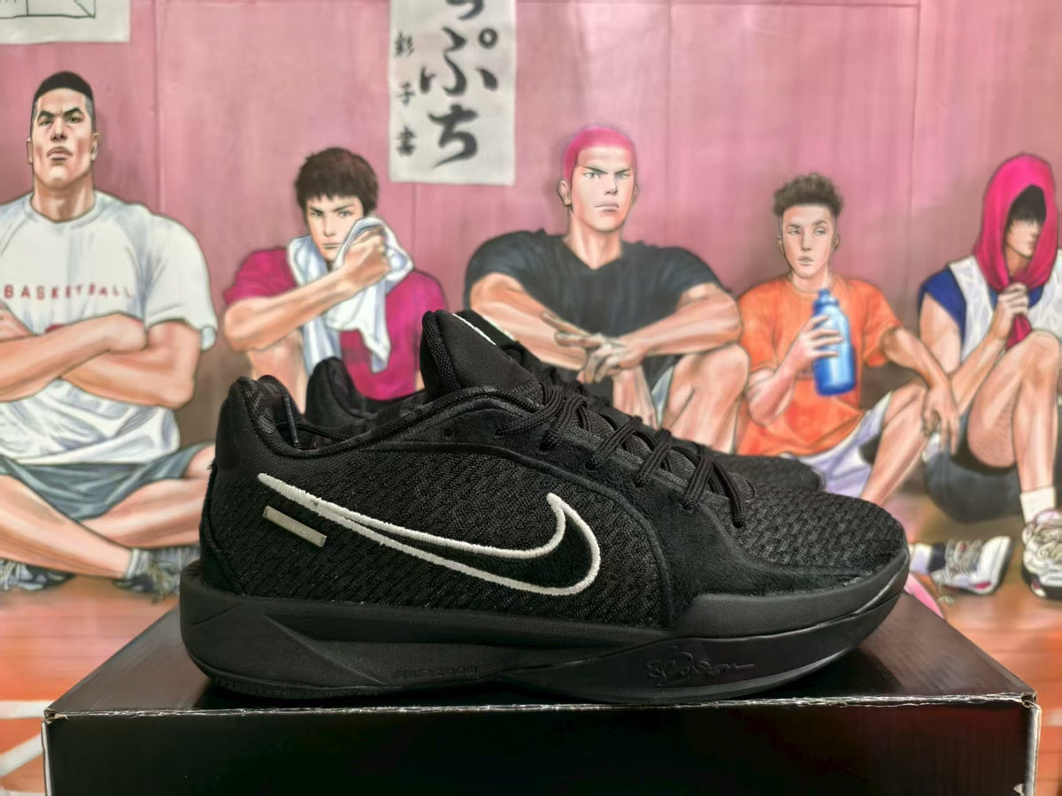 Pair of black Nike sneakers displayed on a shoebox, showing the side profile and light-colored Swoosh detail.