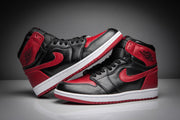Angled view of a pair of black and red high-top sneakers with black laces, red overlays, and white midsoles.