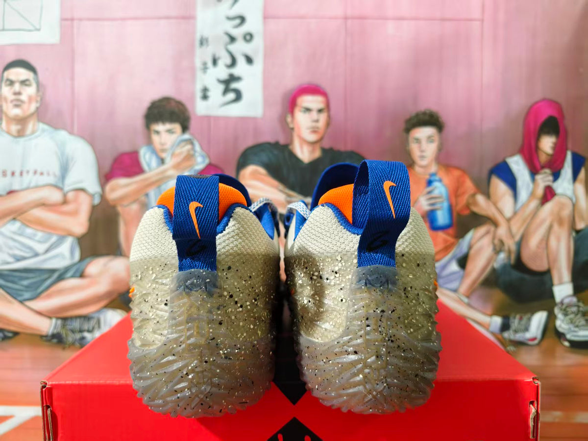 Rear view of beige Nike sneakers with blue and orange details and translucent speckled outsoles on a red shoebox.