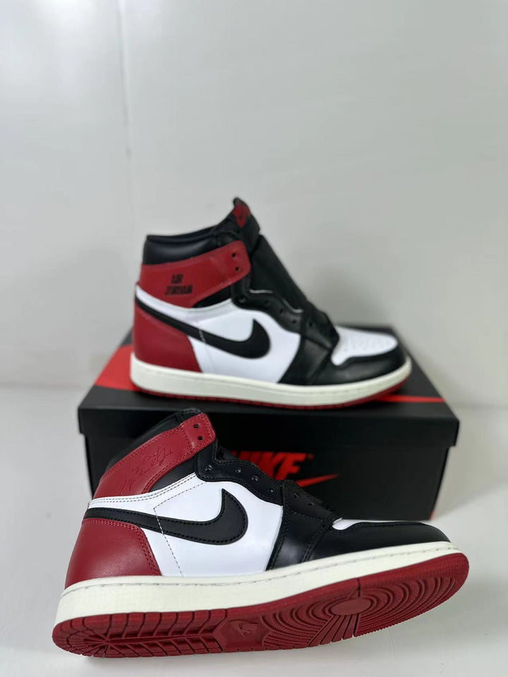 Black, white, and red high-top Jordan sneaker shown from the side with a second shoe and shoebox.