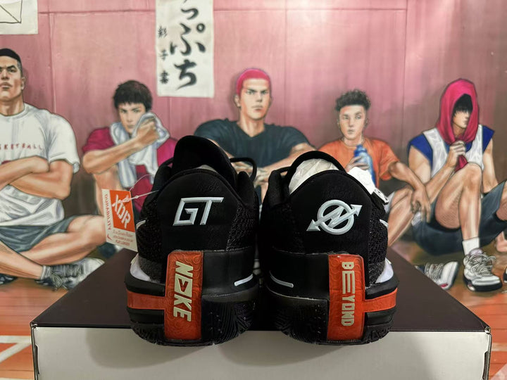 Rear view of black Nike basketball shoes with silver heel logos and orange heel accents.