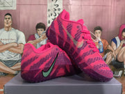 Three-quarter view of paired pink Nike basketball sneakers showing the textured upper, green Swoosh, laces, and translucent outsole.