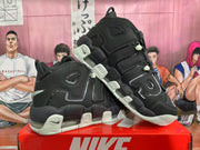 Angled view of paired black Nike basketball sneakers highlighting the layered side design, grey-green sole accents, and translucent cushioning windows.