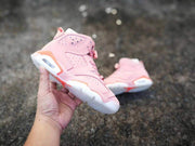 A hand holds one pink Air Jordan 6 sneaker while the matching shoe rests in the background.