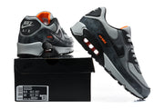 Grey and black Nike Air Max 90 sneakers shown from the rear and side, with a box label visible.