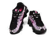 Pair of Nike Shox TL sneakers shown from the front with black laces and pink details.